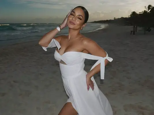 Vanessa Hudgens posing in white off the shoulder dress on a beach