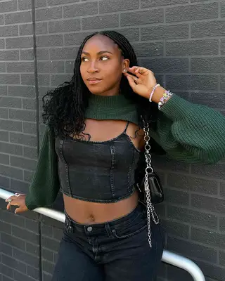 Coco Gauff in a black denim outfit, her hand to her ear 