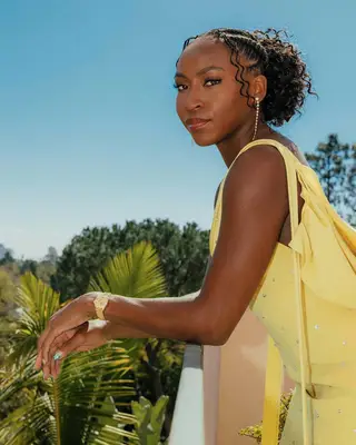 Coco Gauff leaning on a sunny balcony in a yellow dress