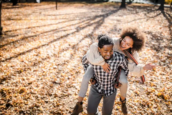 Cheerful African American couple piggybacking in autumn at the park.