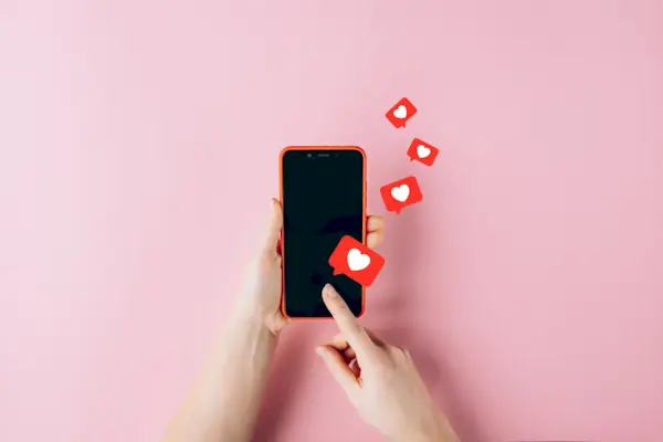 Female hands holding red mobile phone with many social media likes on pink background