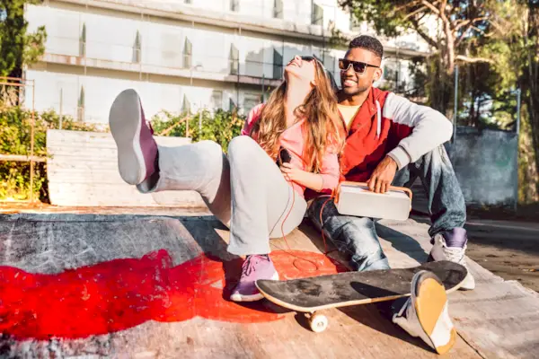 Multiracial couple having fun together at skate park with music boombox - Urban life style concept with genuine people outdoors at love story beginnings - Sunny day with warm contrasted filtered tones