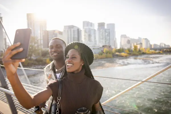 Happy young couple taking selfie on sunny city footbridge over river