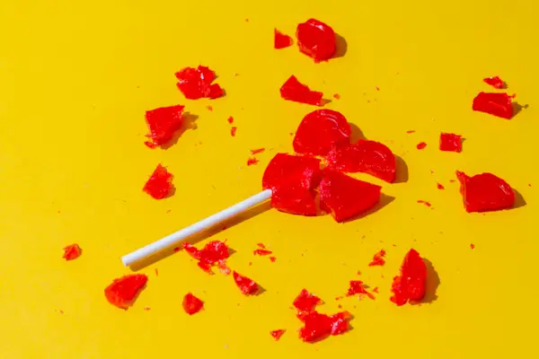Broken Red Heart-Shaped Lollipop On Yellow Background