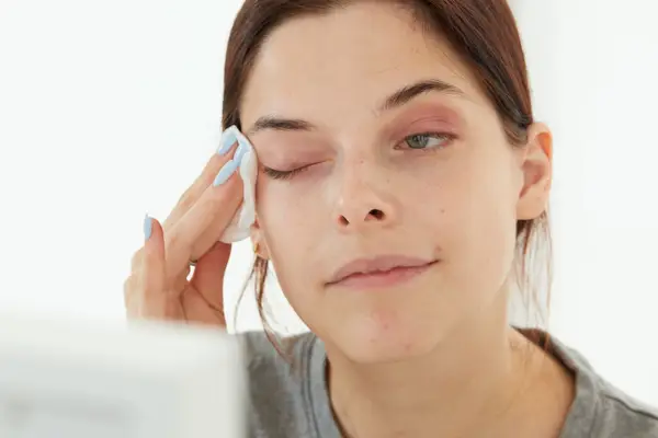 A person wiping eye makeup off using Glossier Milky Oil on a cotton round 