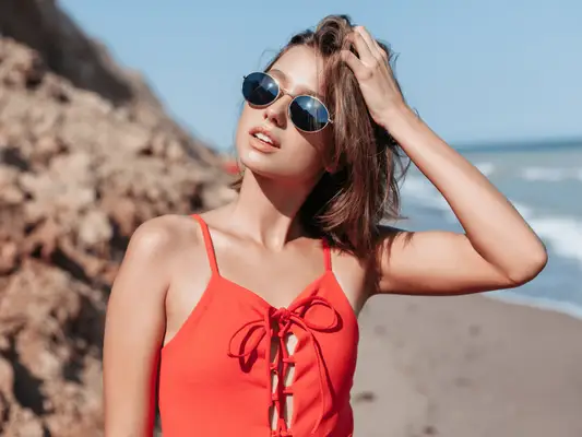 Image of a woman on the beach in a bathing suit and sunglasses with her face to the sun