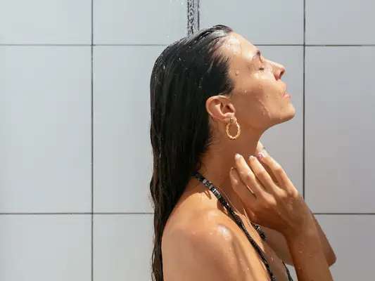 Woman in shower with tile background and gold hoop earrings
