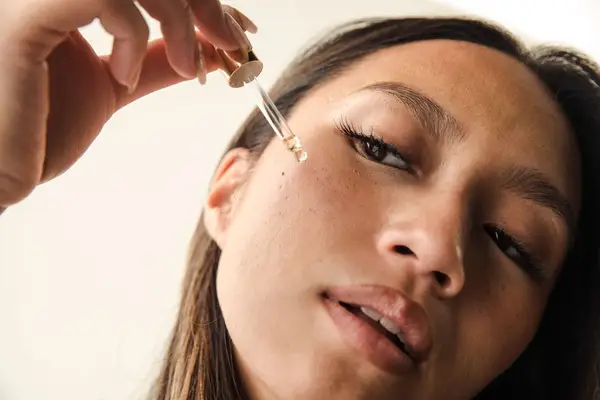 Woman applying a serum, head to the side looking downward.