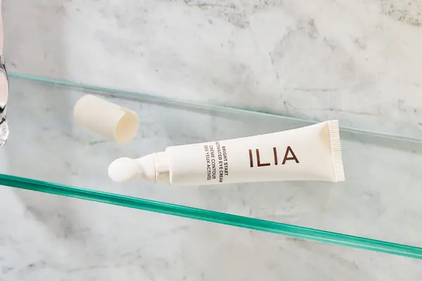 Tube of ILIA Bright Start Retinol Alternative Brightening Eye Cream on a glass shelf. 