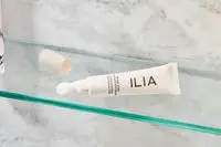 Tube of ILIA Bright Start Retinol Alternative Brightening Eye Cream on a glass shelf. 