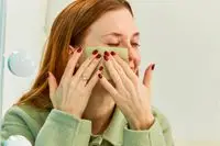 Hands using blotting paper on cheek
