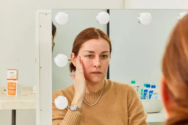 Face reflected in mirror as hand rubs sunscreen onto cheek