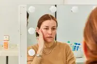Face reflected in mirror as hand rubs sunscreen onto cheek