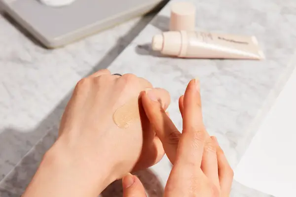 Hand dabbing Iris & Romeo Weekend Skin SPF 50 + Vitamin C + Glow onto other hand over marble counter