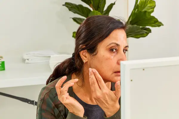 Person rubbing sunscreen onto face while looking in mirror