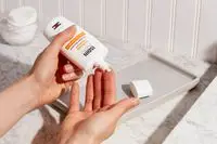Hand dispensing Isdin Eryfotona Actinica Mineral SPF 50+ Sunscreen onto other hand with nearby tray and marble countertop
