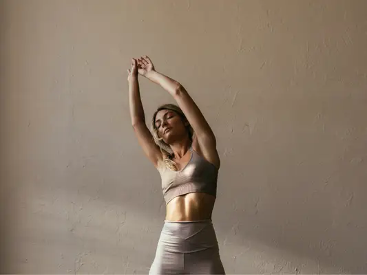 A woman in workout clothes stretching her arms up above her head