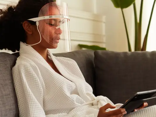 A woman wearing an LED light therapy mask and a bathrobe