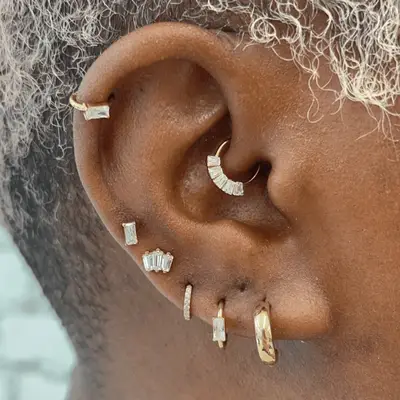 An ear with mismatched gold baguette diamond earrings.
