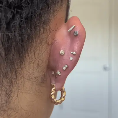 Close up of the back of an ear with assorted decorative earring backs displayed.