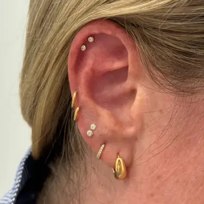 An ear with gold and diamond mismatched earrings, including two sets of round snakebite studs.