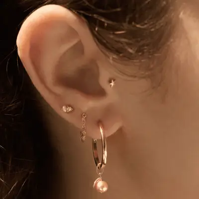 Close up of an ear with multiple earrings, including two pearl studs, a star stud, and a pearl drop hoop earring.