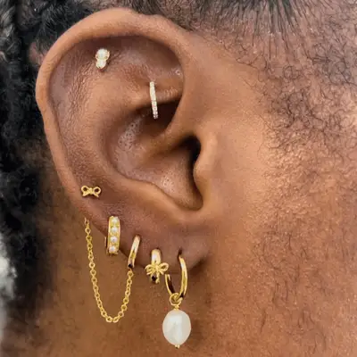 Close up of an ear with a gold earring stack including bow studs, pearl hoops, and diamond studs.