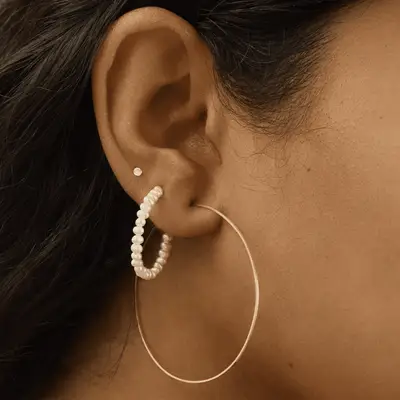 Close up of an ear with a large gold and pearl hoop earring stack, with an accent gemstone stud.