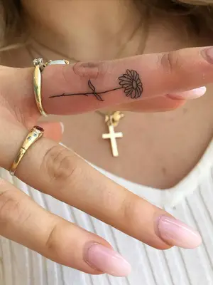 close up of tiny flower tattoo in black ink on side of middle finger