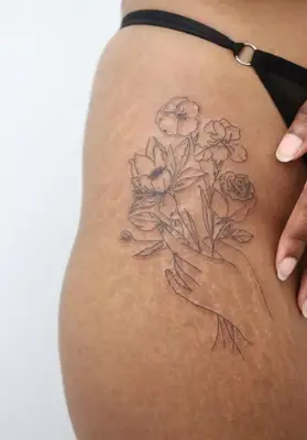 A tattoo on an upper thigh depicting a hand holding a bouquet of flowers