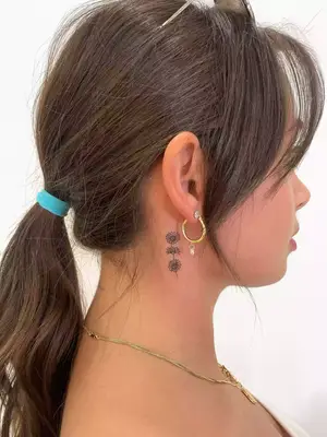 close up of black ink tattoo of three small flowers placed vertically behind ear