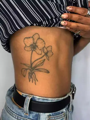close up of black ink tattoo on ribcage of two orchids