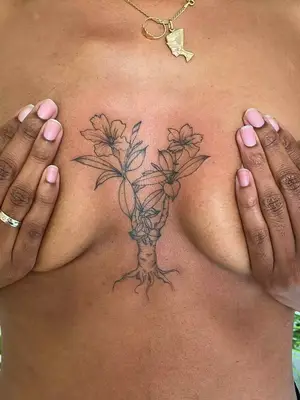 close up of desert rose tattoo in black ink on chest in between breasts, with trunk and flowers coming out of it
