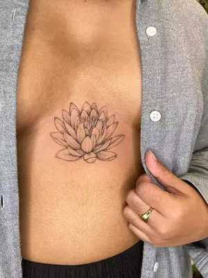 close up of water lily black ink tattoo on upper stomach