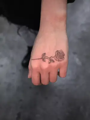 close up of black ink rose tattoo on hand placed horizontally above fingers