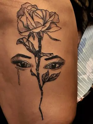 close up of black ink tattoo of large flower with stem and realistic crying eyes with eyebrows behind it, looking through