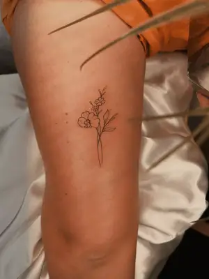 close up of black ink tattoo of small flower bunch on upper arm