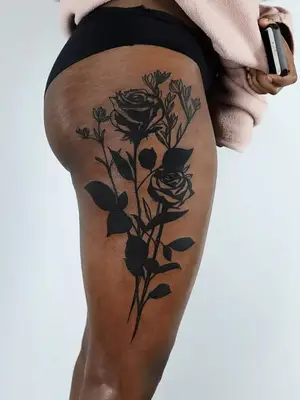close up of black ink tattoo of large roses and flowers covering entirety of side of thigh from knee to hip