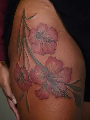close up of hip tattoo of red tropical flowers with green stems, facing upside down on upper thigh and hip