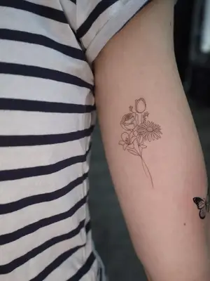 close up of black ink tattoo on upper arm of flower bundle with 4 different types of flowers, small in size