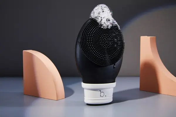 Three facial cleansing brushes set up against a gray background