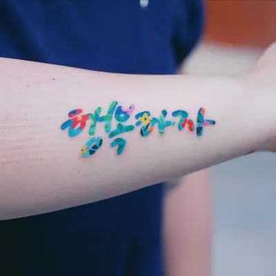 Colorful floral Korean lettering tattoo on forearm