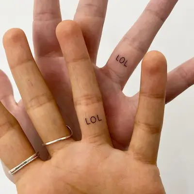 Matching LOL word tattoos on inner ring finger