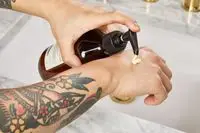 person pumping Aesop Geranium Leaf Body Balm onto back of hand