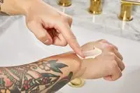 person rubbing Aesop Geranium Leaf Body Balm onto back of their hand 