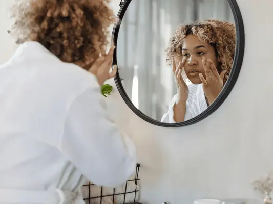 A woman in a robe looking in the mirror and touching her face with her hands