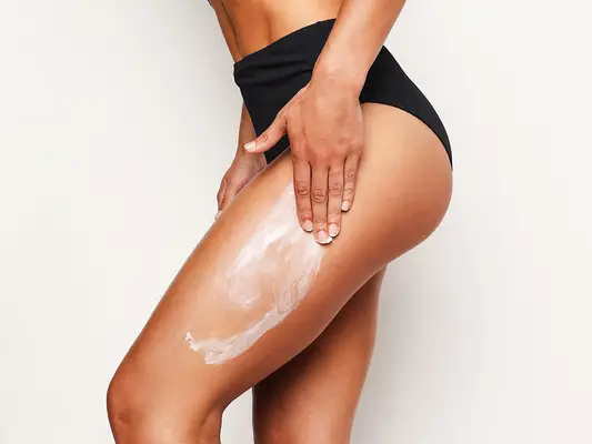 woman wearing a black swimsuit applying a white body cream on her leg