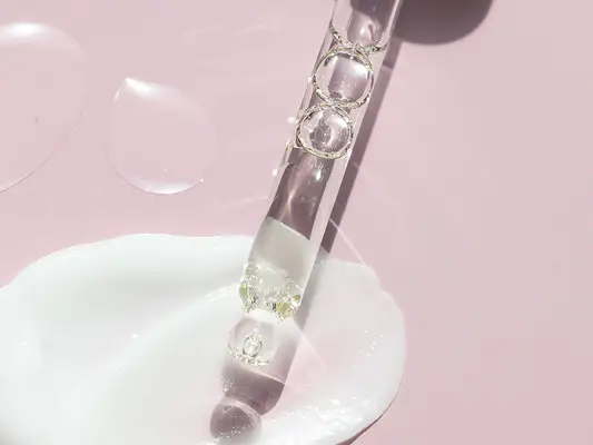 Close up of a liquid in a dropper, against a swatch of cream