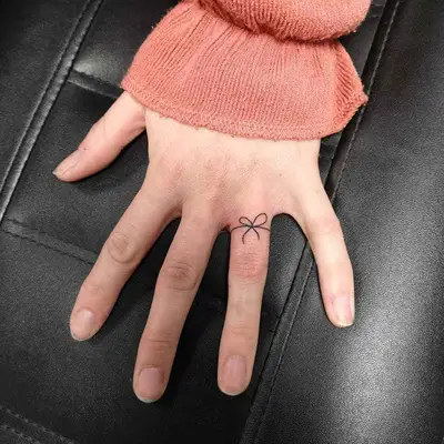 Person with a minimalist bow ring finger tattoo