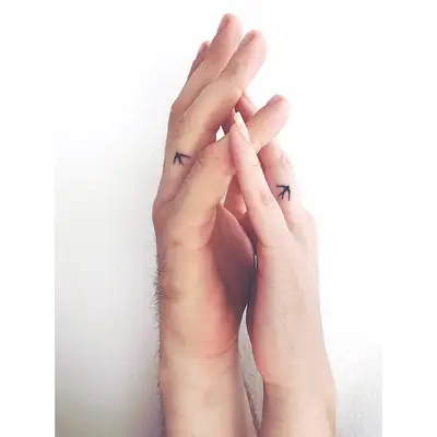 Two people with matching bird ring finger tattoos